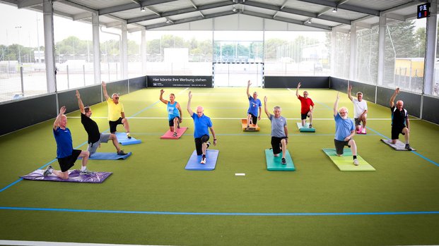 "Gemeinsam Aktiv: Fitness für Senioren im Freien" Ältere Menschen machen Gymnastik auf bunten Matten in einer überdachten Sporthalle.