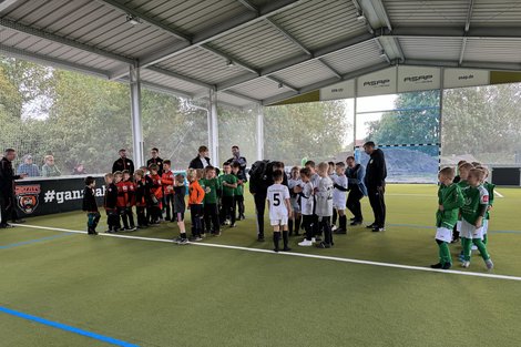 Kinderfußballteams versammeln sich in einer Halle auf einem Kunstrasenplatz, um Anweisungen von ihren Trainern zu erhalten.