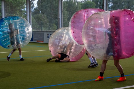 "Ausgelassener Spaß beim Bubble-Fußballspiel" Mehrere Personen spielen Bubble Soccer in aufblasbaren Bällen auf einem Rasenplatz.