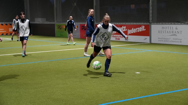 "Intensives Training unter Flutlicht: Frauenfußball auf dem Kunstrasen" Personen spielen abends auf einem Kunstrasen-Fußballplatz. Eine Person dribbelt den Ball nah am Boden.
