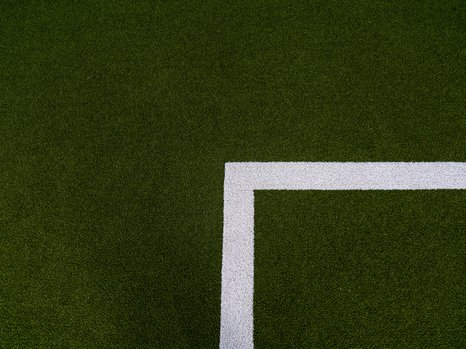 Ein grüner Kunstrasen mit einer weißen, rechteckigen Begrenzungslinie in der unteren rechten Ecke des Bildes, die einen Teil eines Sportfeldes darstellt.