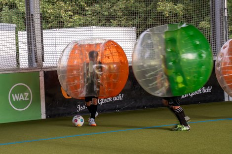 "Bubble-Soccer: Spiel, Spaß und Kollisionen auf dem Spielfeld" Menschen spielen Bubble Soccer in einem überdachten Spielfeld; sie tragen große, aufblasbare Kugeln.