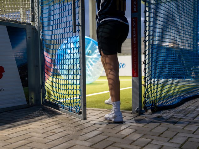 Barrierefreier Zugang Person verlässt Spielfeld durch ein Tor mit blauen Netzen, Hintergrund zeigt aufgeblasene Kugel.
